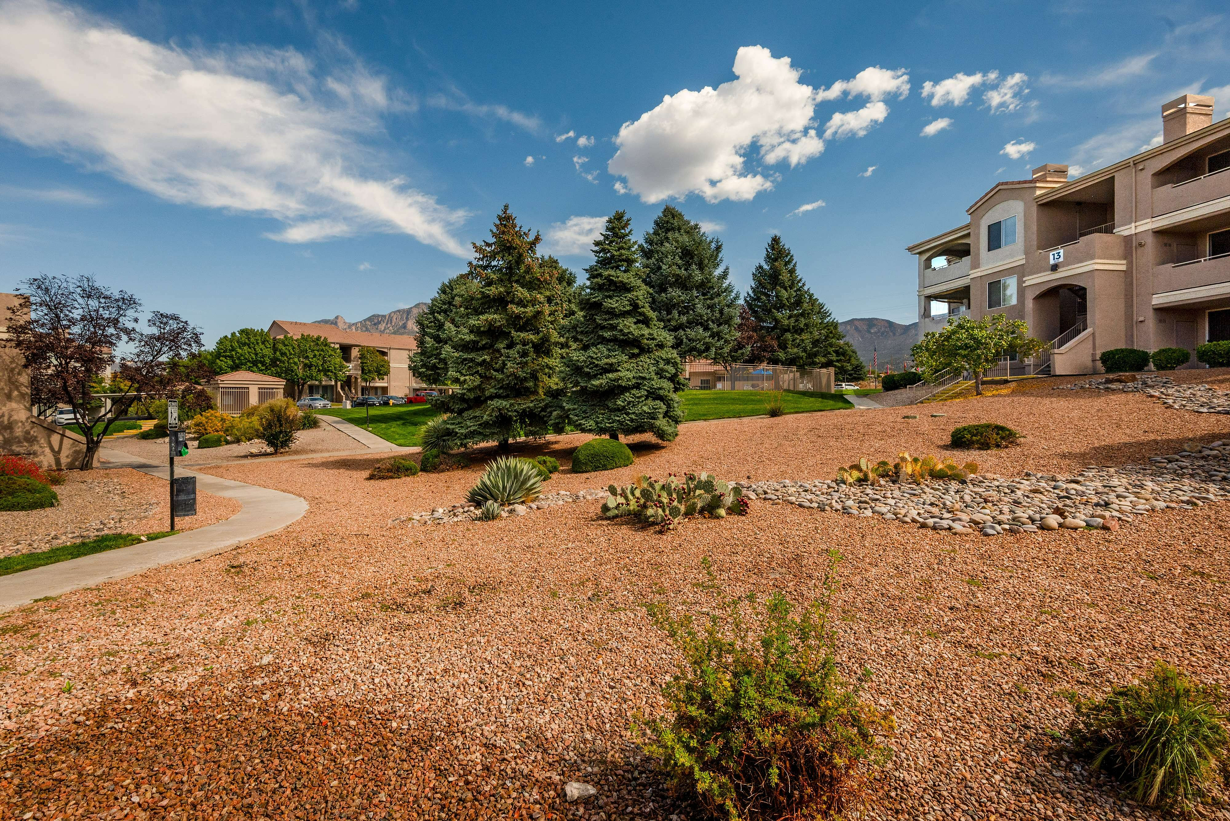 Beautiful apartment complex surrounded by lush greenery, manicured landscaping, and scenic mountain views under a vibrant blue sky.