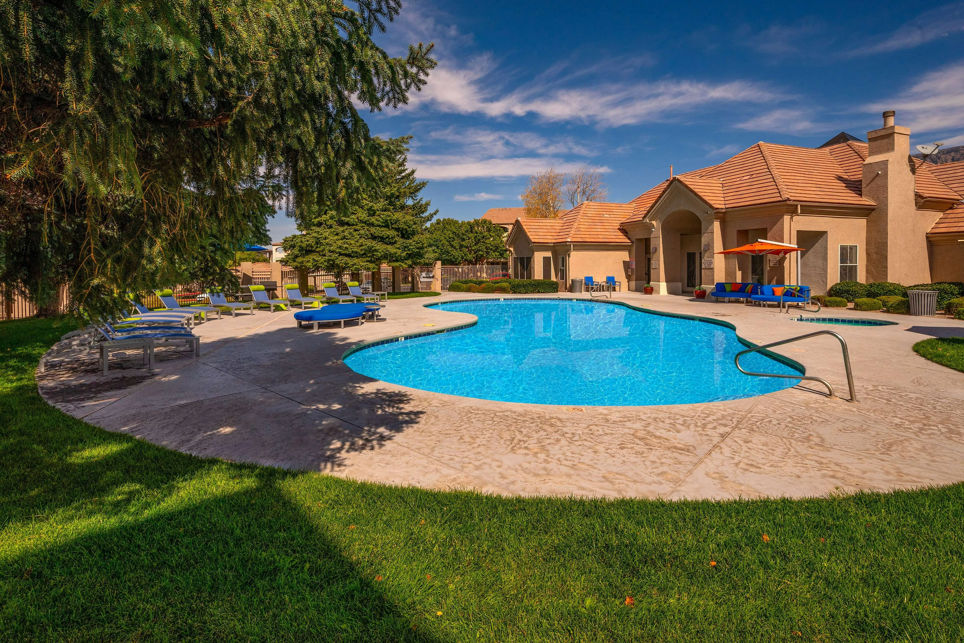 Luxurious apartment complex with a stunning outdoor pool surrounded by lush greenery and stylish lounge chairs.