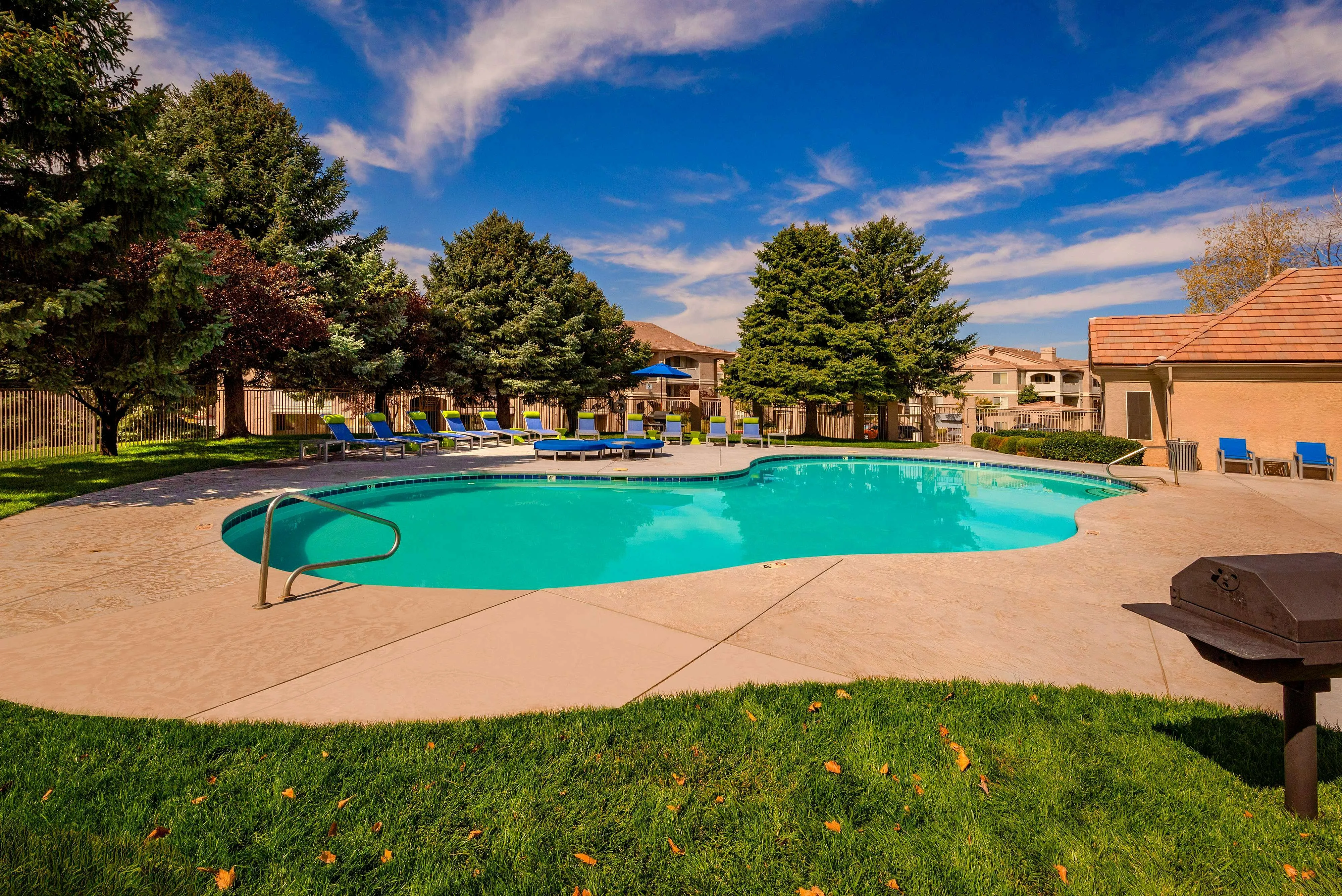 Inviting outdoor pool surrounded by lush greenery and comfortable lounge chairs under a clear blue sky.