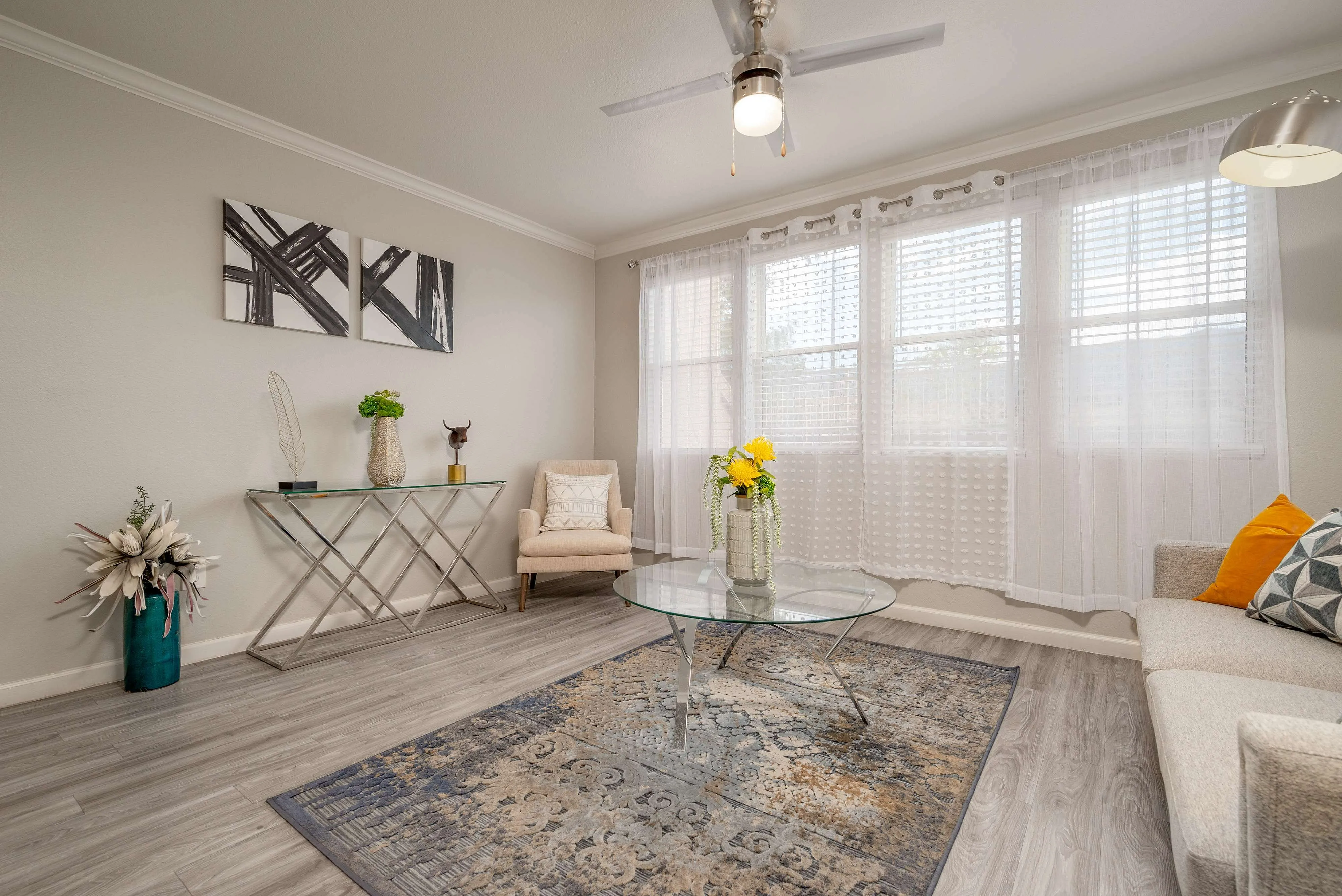 Bright and modern living room with elegant decor, featuring a stylish glass coffee table, cozy seating, and large windows for natural light.