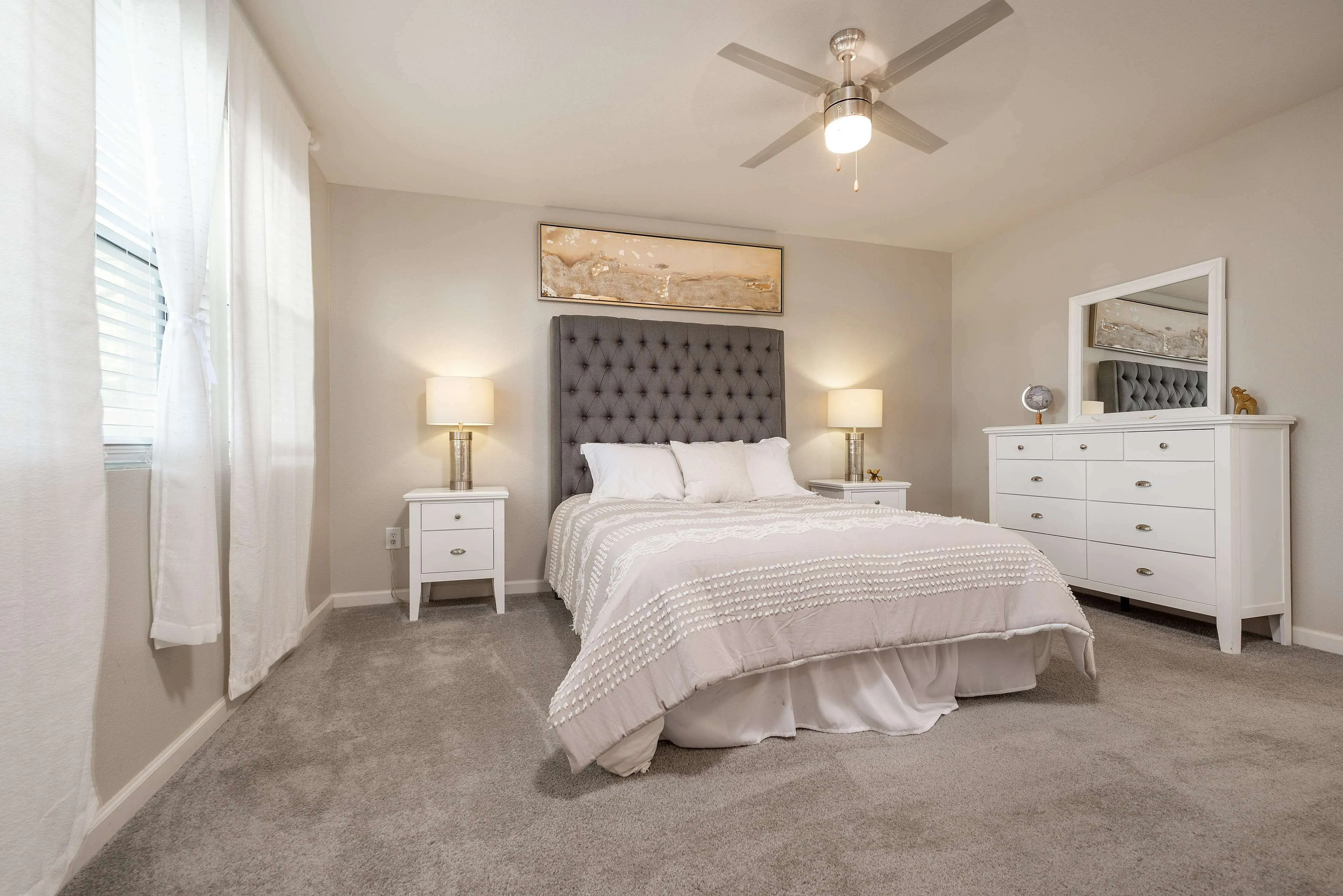 Elegant bedroom featuring a plush gray headboard, soft lighting, and crisp white furnishings creating a serene retreat.
