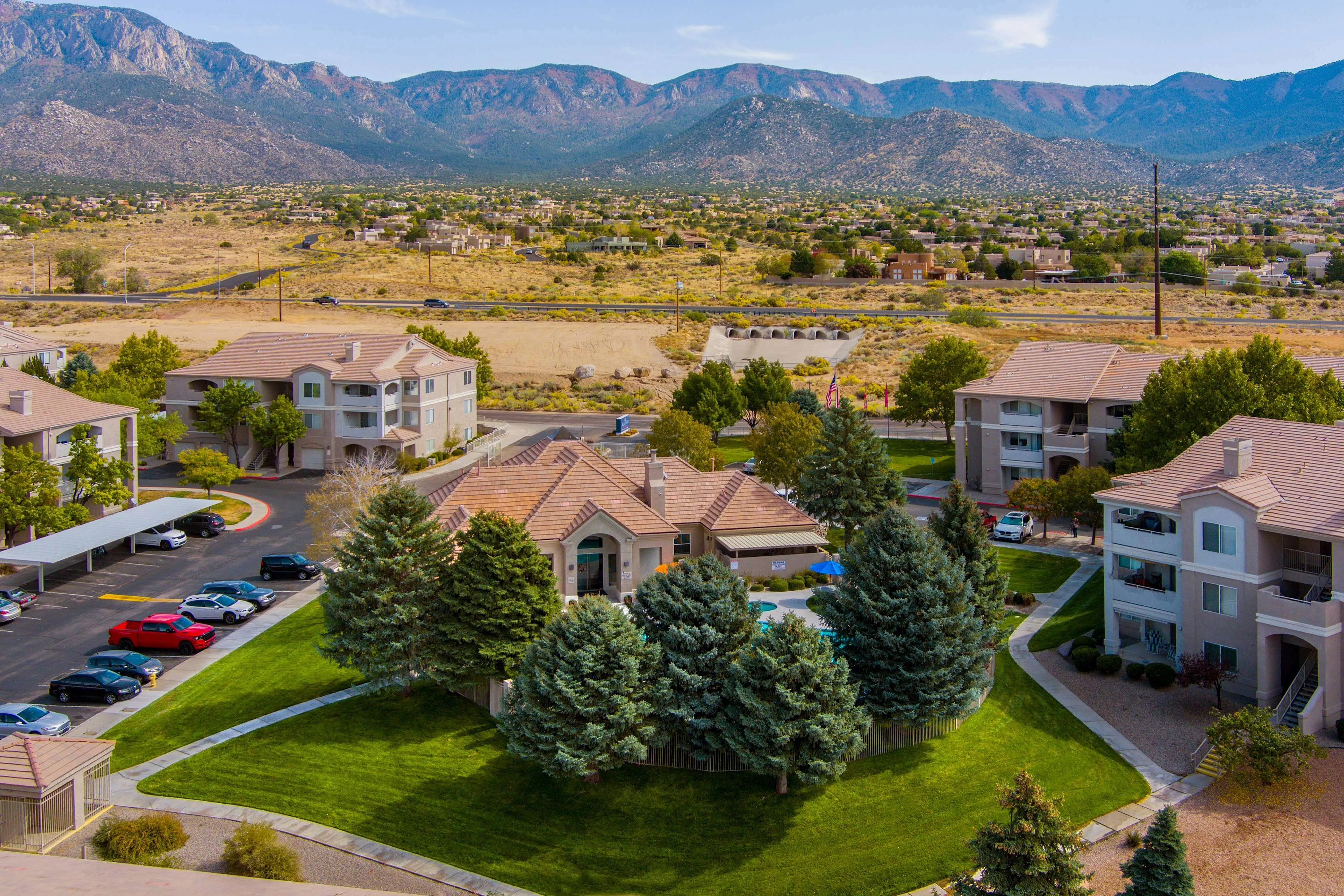 Captivating aerial view of a serene apartment complex with lush landscaping, communal swimming pool, and stunning mountain backdrop.