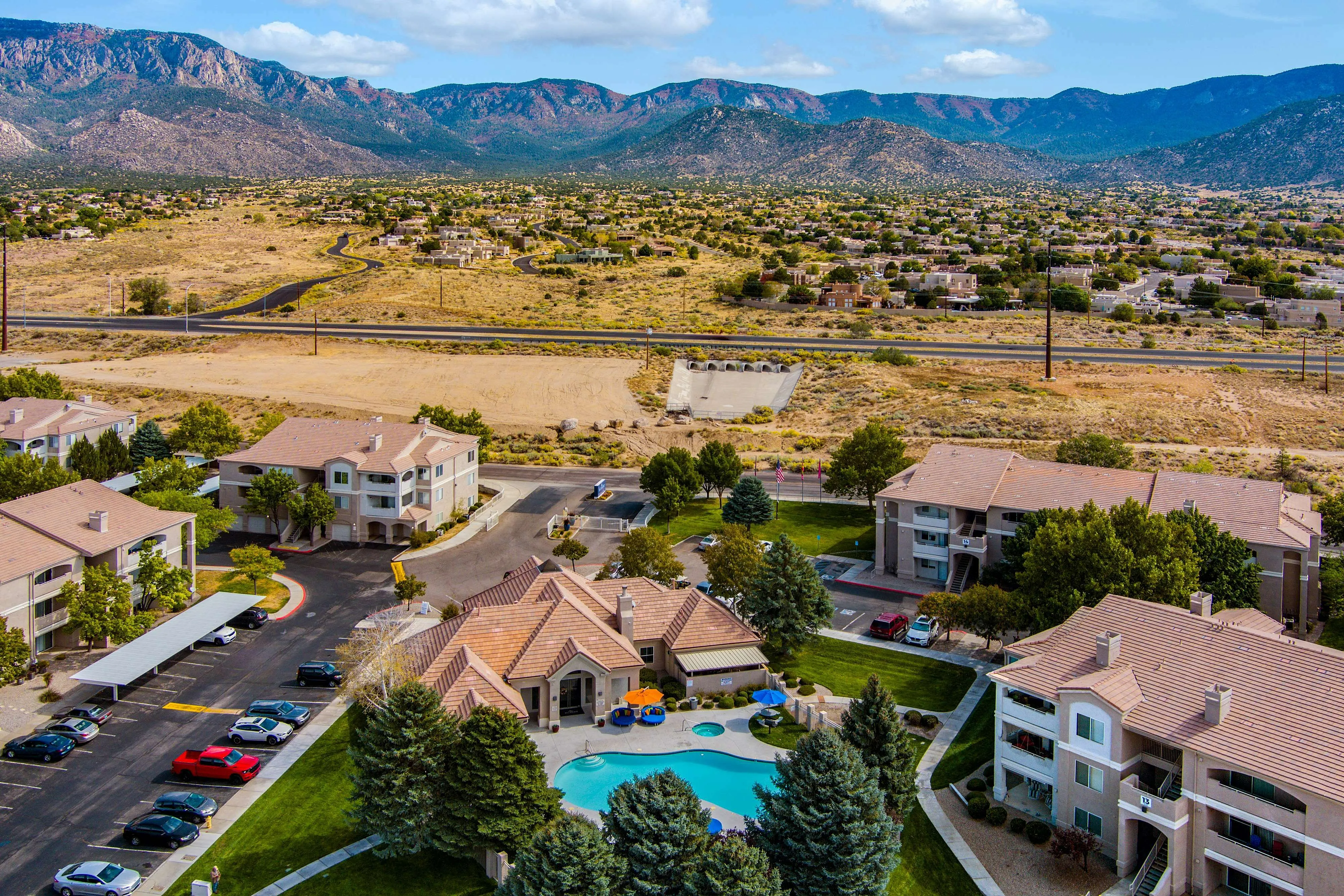 Scenic aerial view of a charming apartment community with a sparkling swimming pool, nestled at the base of breathtaking mountains, offering serene and picturesque living.
