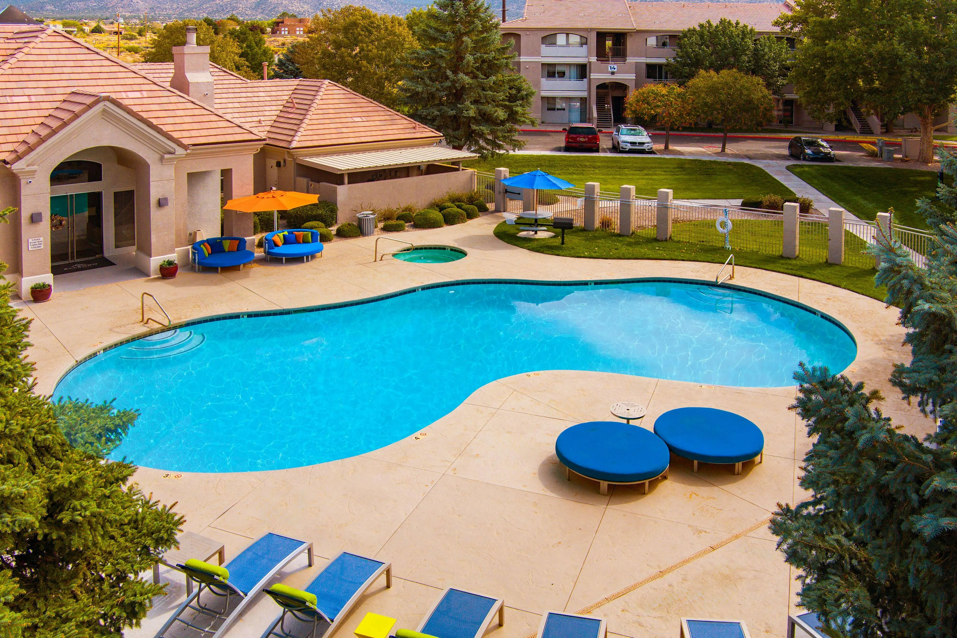 Elegant apartment community featuring a sparkling outdoor pool with stylish lounge areas and vibrant umbrellas, surrounded by lush greenery.