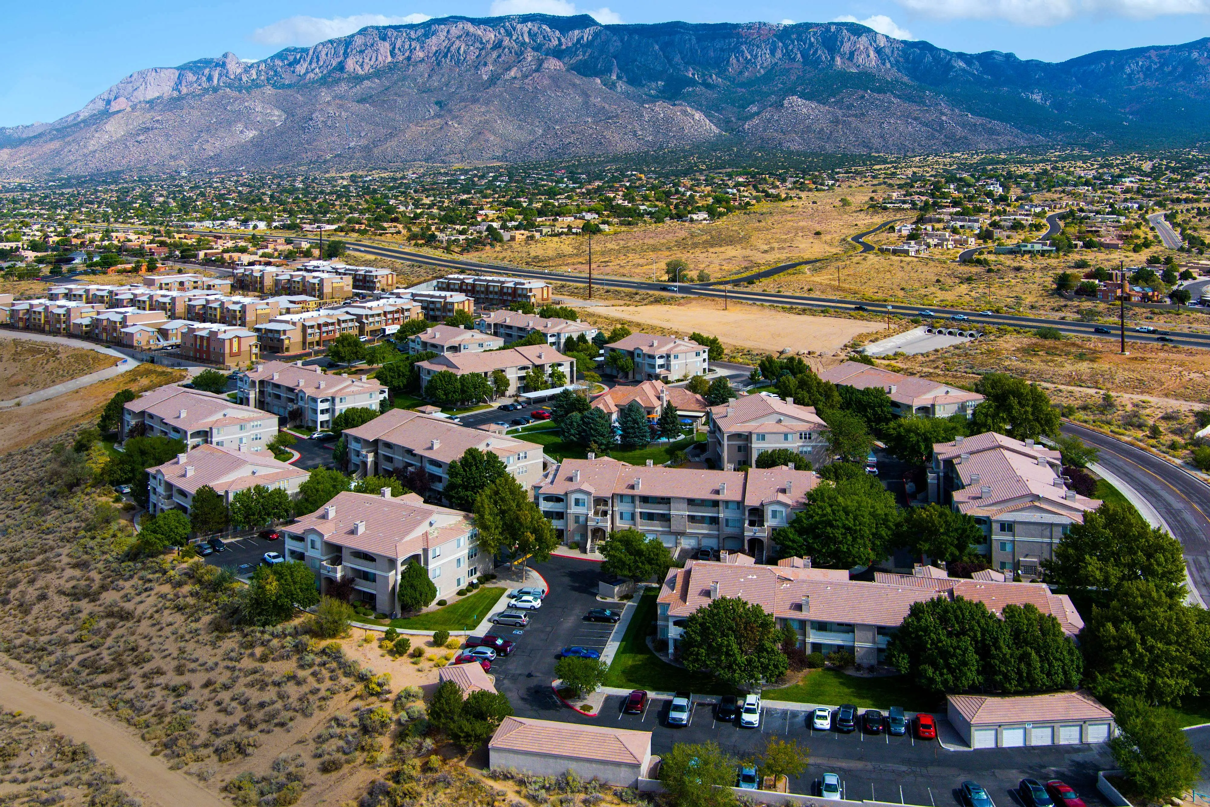Stunning aerial view of modern apartment complex nestled in picturesque landscape with mountain backdrop and vibrant greenery.