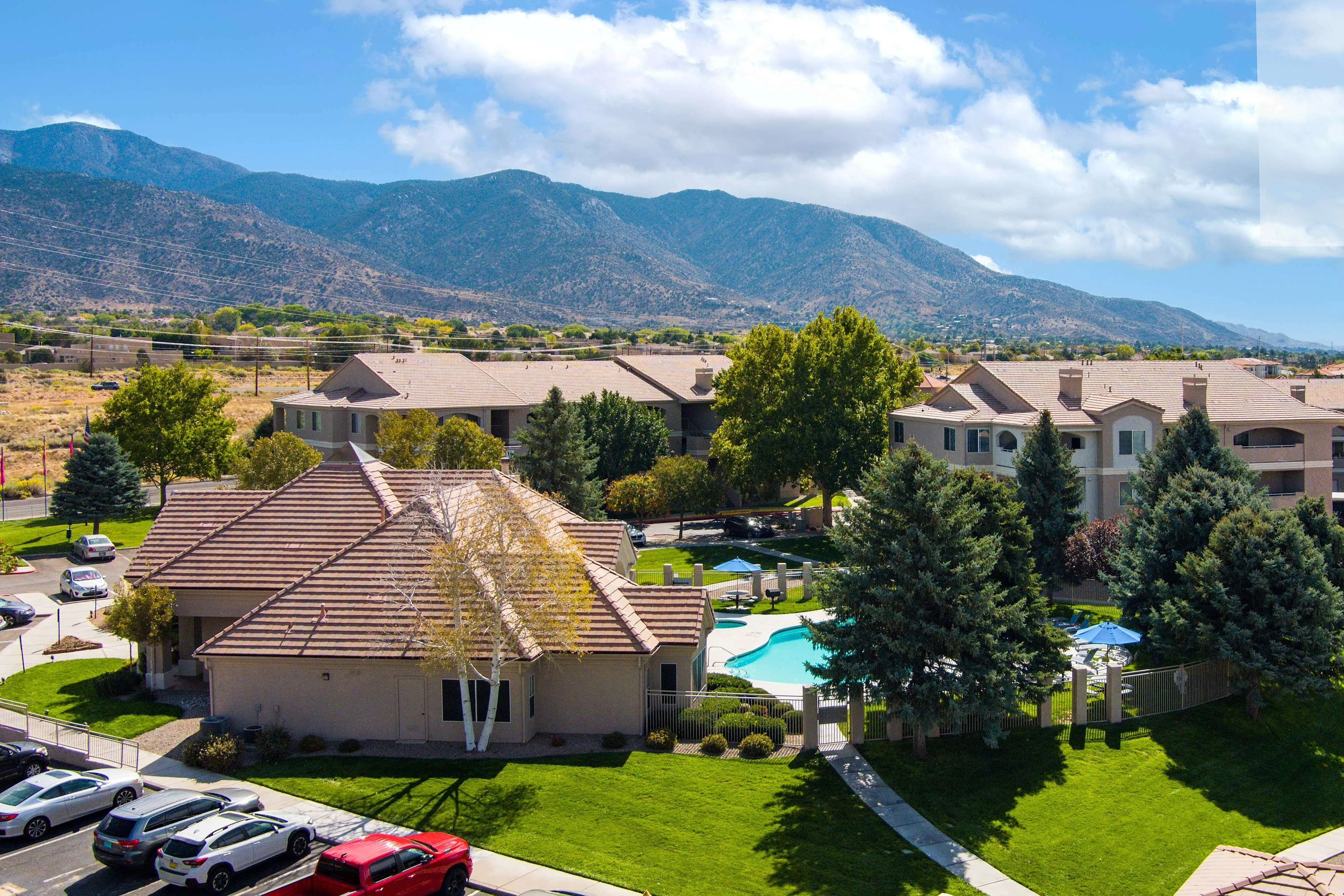 Scenic apartment complex with a sparkling pool and lush landscaping, set against a backdrop of majestic mountains.