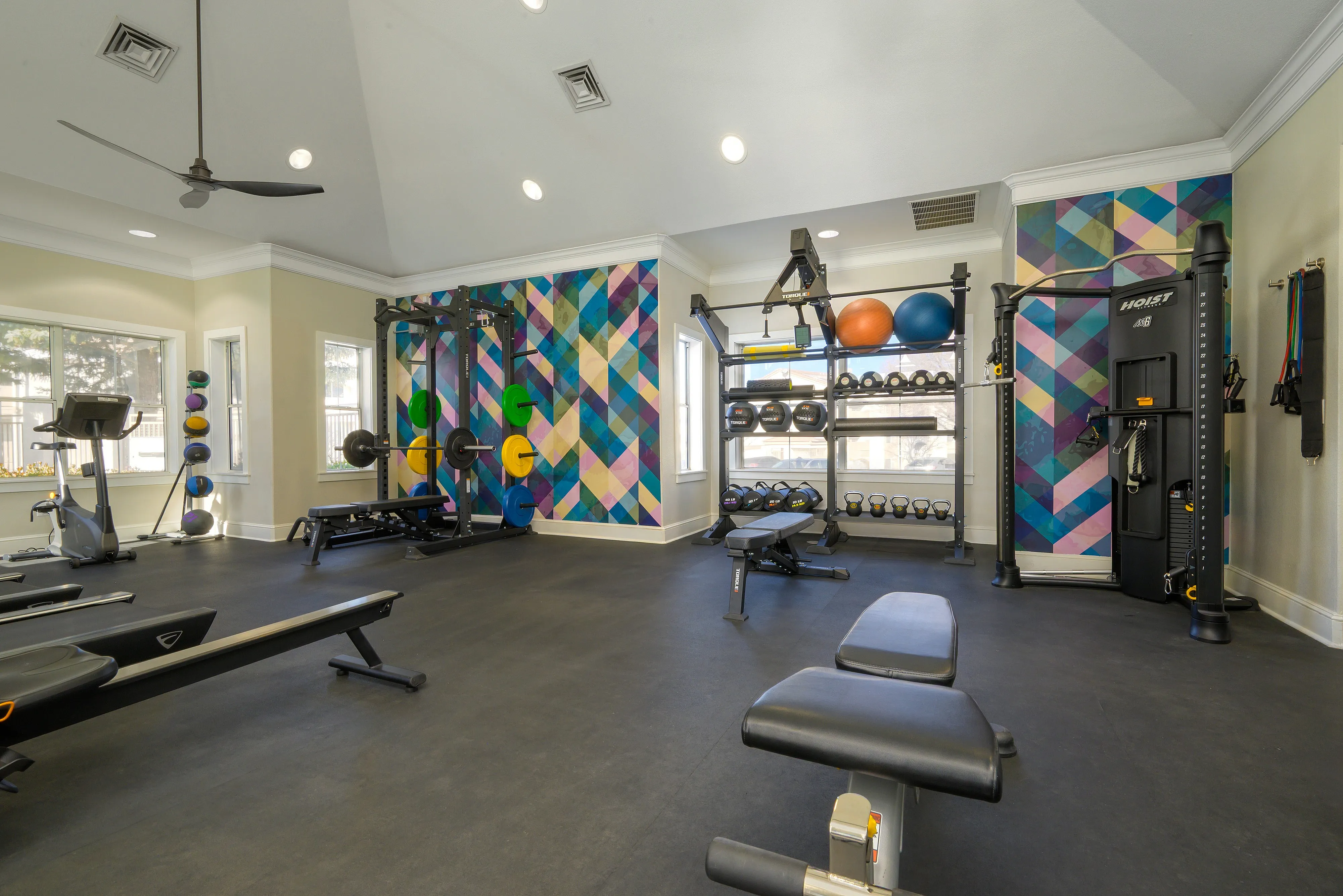 Modern fitness center with colorful geometric wall design, equipped with advanced exercise machines, free weights, and ample natural light.