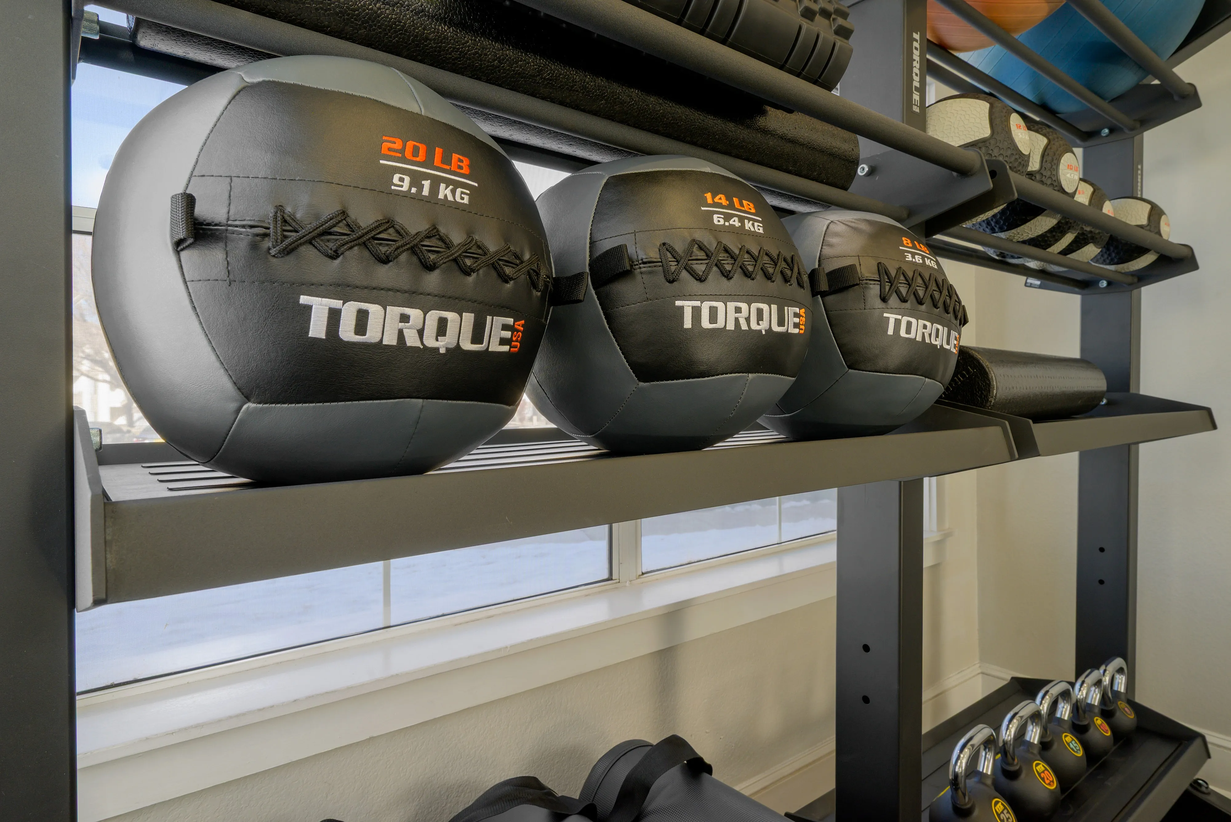 Modern gym features sleek shelves with Torque USA medicine balls and kettlebells, ideal for dynamic workouts in a fitness-focused space.