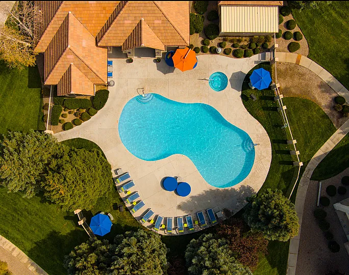 Aerial view of a luxurious apartment complex showcasing a sparkling blue pool, surrounded by lush greenery and sun loungers with vibrant umbrellas.