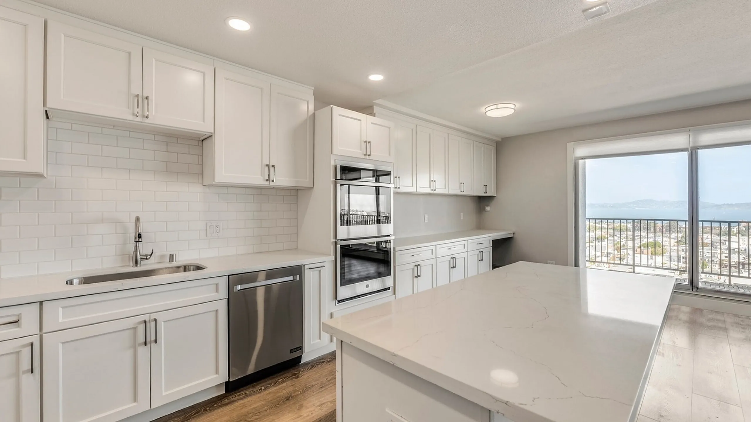 Elegant modern kitchen with sleek white cabinetry, stainless steel appliances, and a stunning island, overlooking a breathtaking cityscape view through large windows.