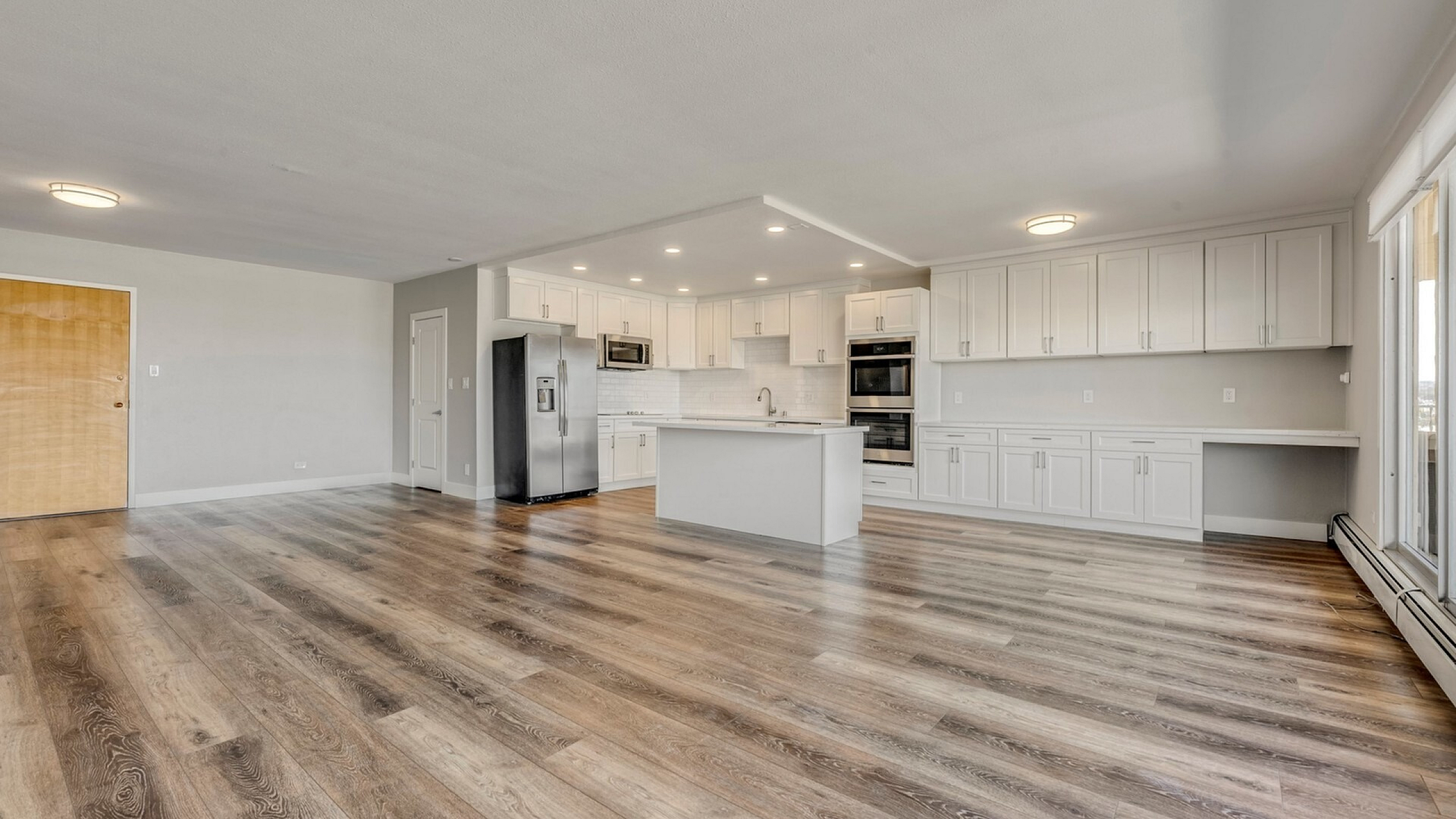 Spacious modern kitchen with sleek appliances, ample white cabinetry, and elegant wood flooring, perfect for entertaining.