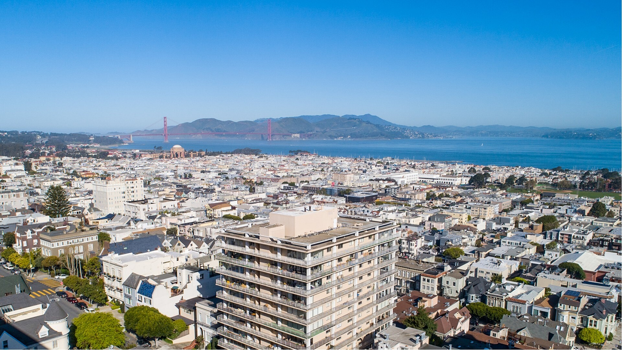 Scenic aerial view showcasing a vibrant cityscape with a modern high-rise, stunning bay backdrop, and iconic bridge, capturing urban beauty and dynamic living.