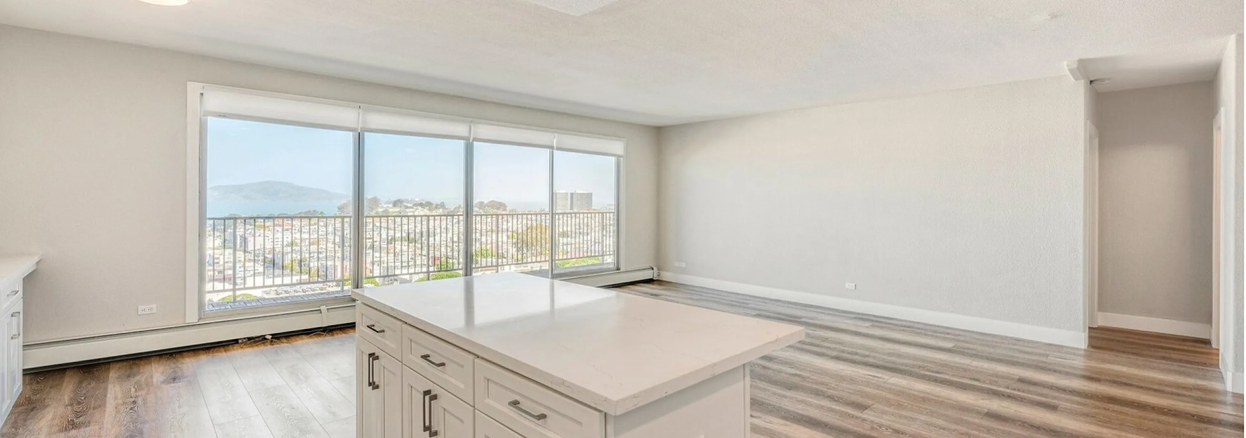 Bright apartment interior featuring a modern kitchen island and expansive windows with breathtaking city and hillside views.