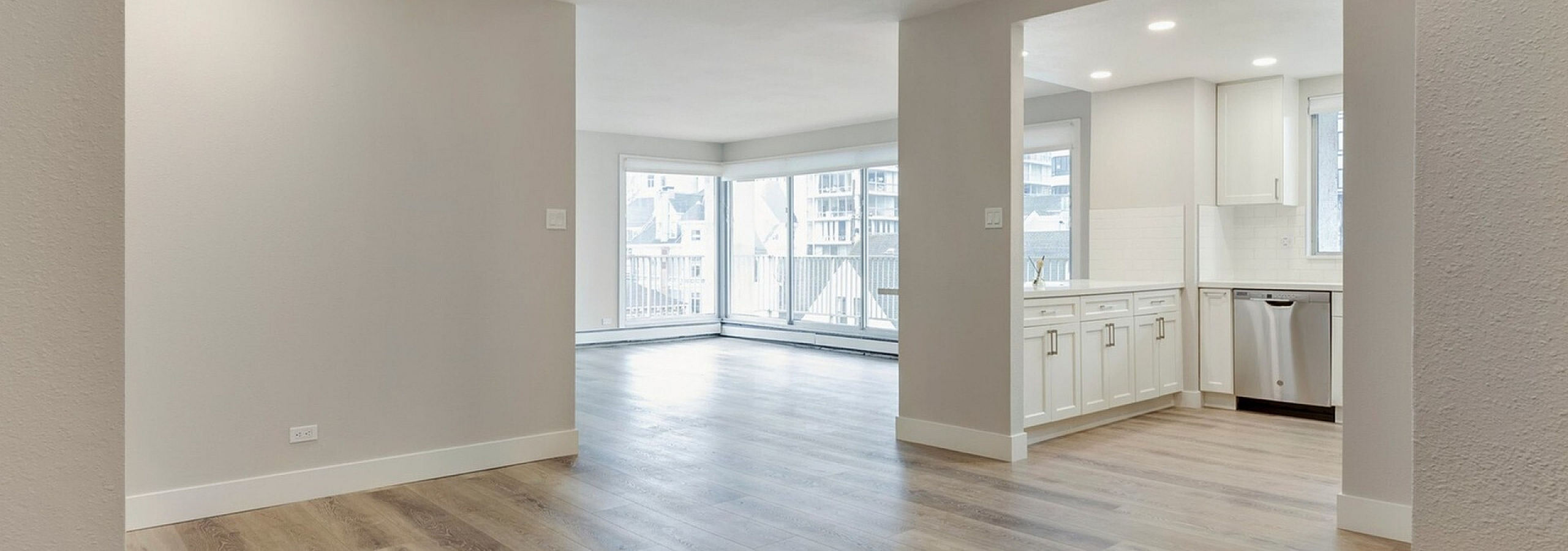Modern apartment with open-concept layout featuring sleek hardwood floors, large windows for natural light, and a chic white kitchen with stainless steel appliances.
