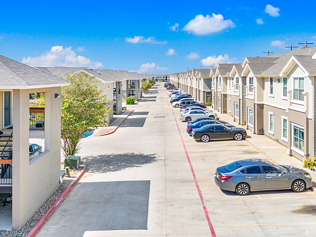 Modern apartment complex with spacious parking, showcasing a bright and inviting atmosphere under a clear blue sky.