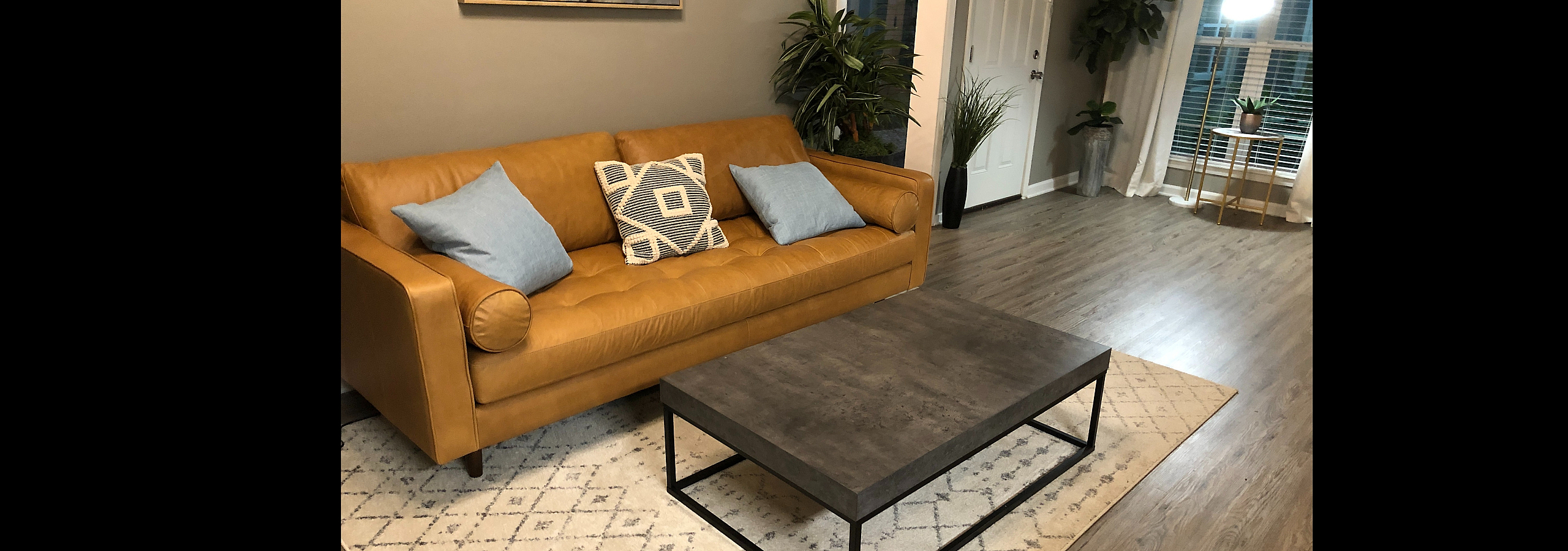 Inviting living room with a stylish tan sofa, modern coffee table, and lush greenery, perfect for relaxation.