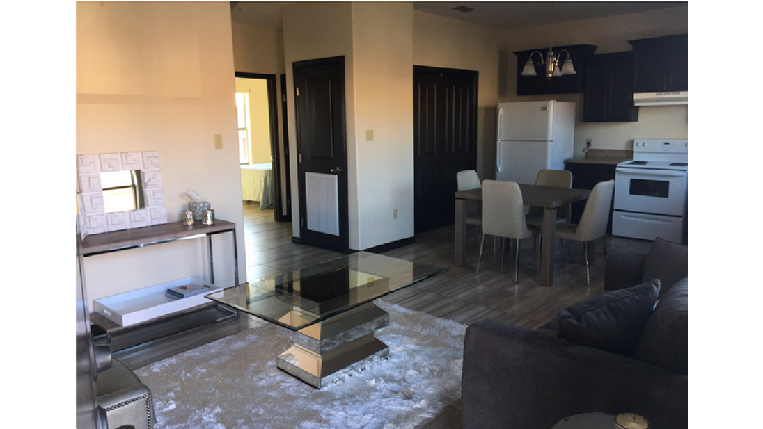 Modern open-plan living room with elegant glass coffee table, cozy seating, dining area, and sleek kitchen appliances.