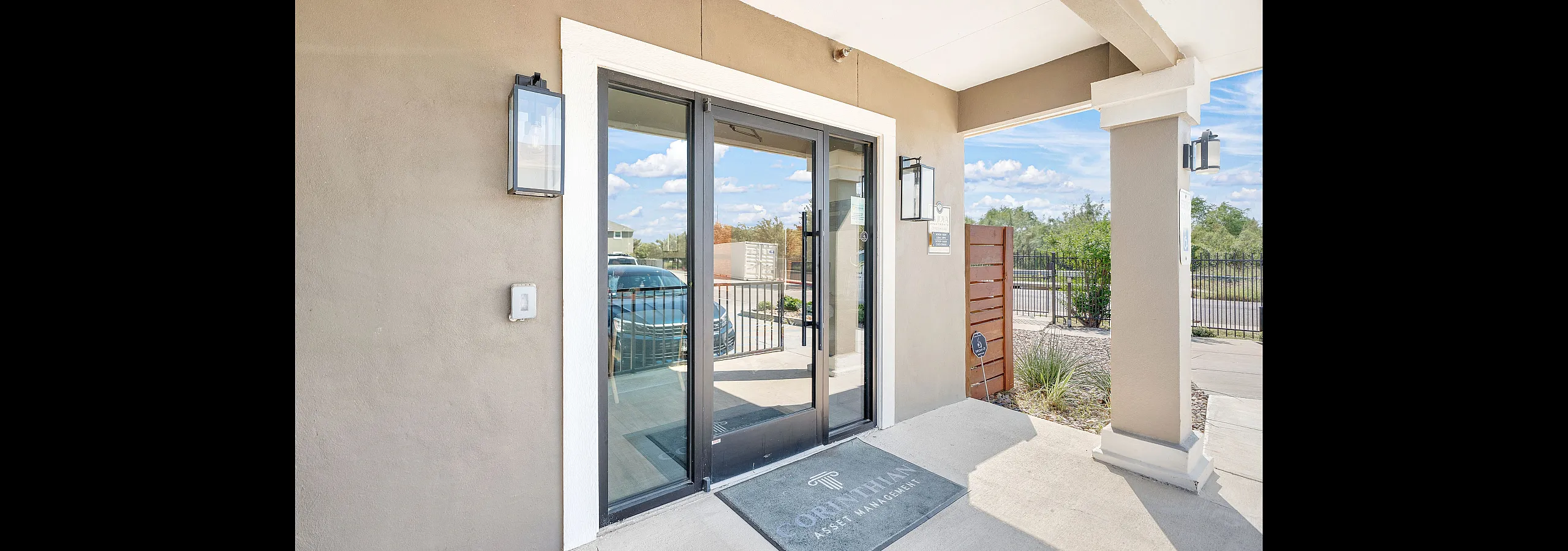 Inviting modern entrance with glass doors, elegant lighting, and a view of lush greenery and clear skies beyond.