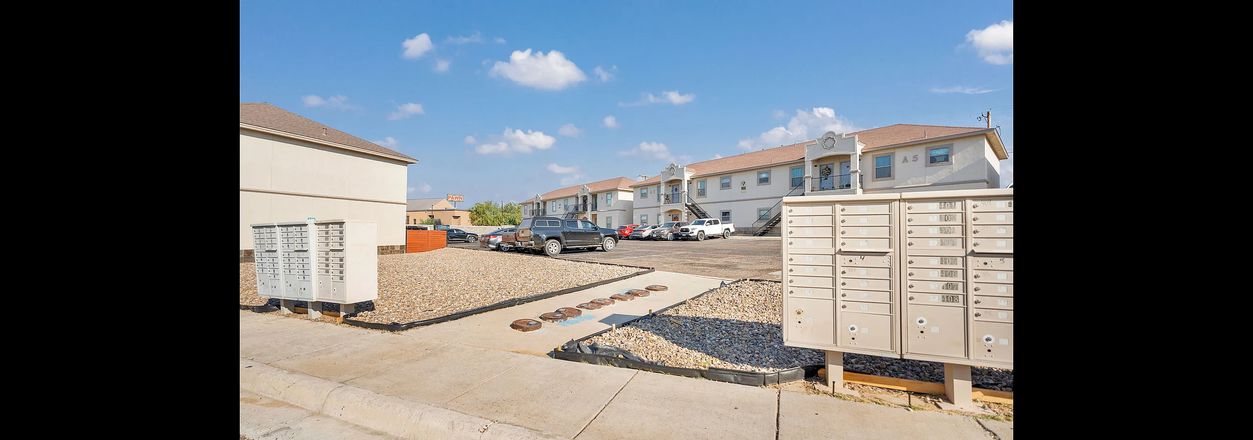 Charming apartment complex with convenient parking and mailbox area under a bright blue sky.