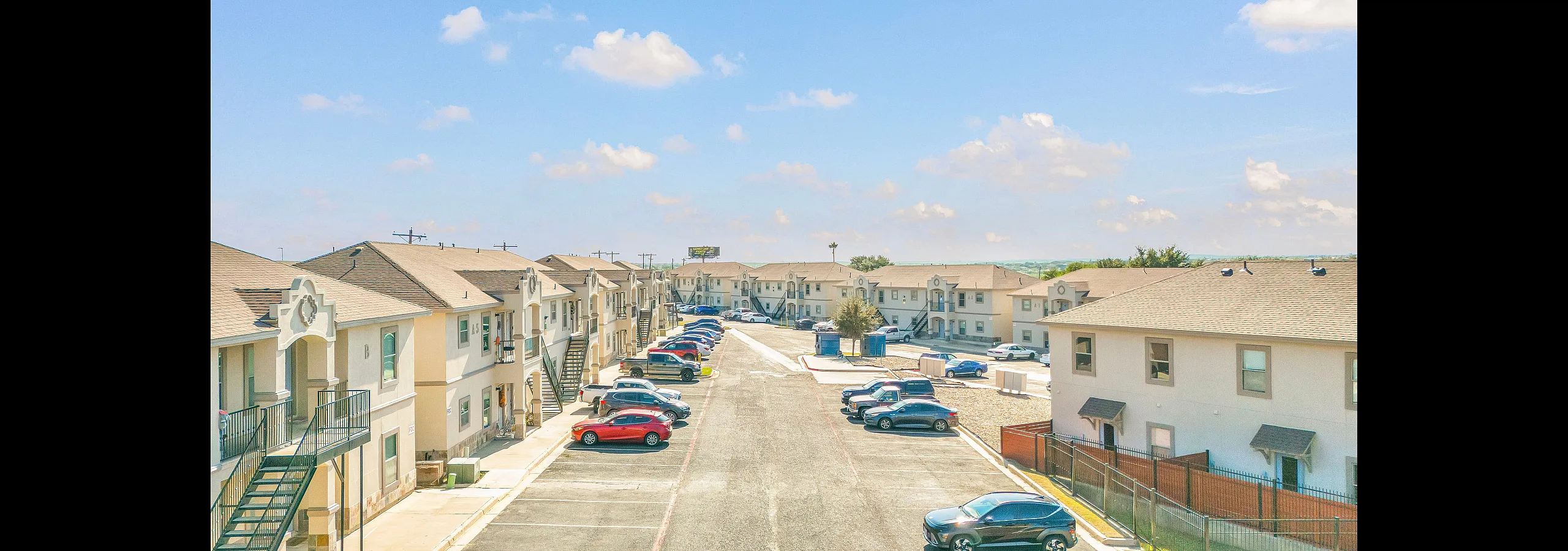 Modern apartment complex with stylish architecture, ample parking, and a bright, clear sky enhancing the inviting atmosphere.