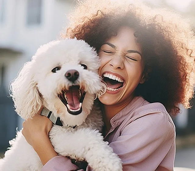 Joyful woman with curly hair laughing while hugging a playful white fluffy dog.