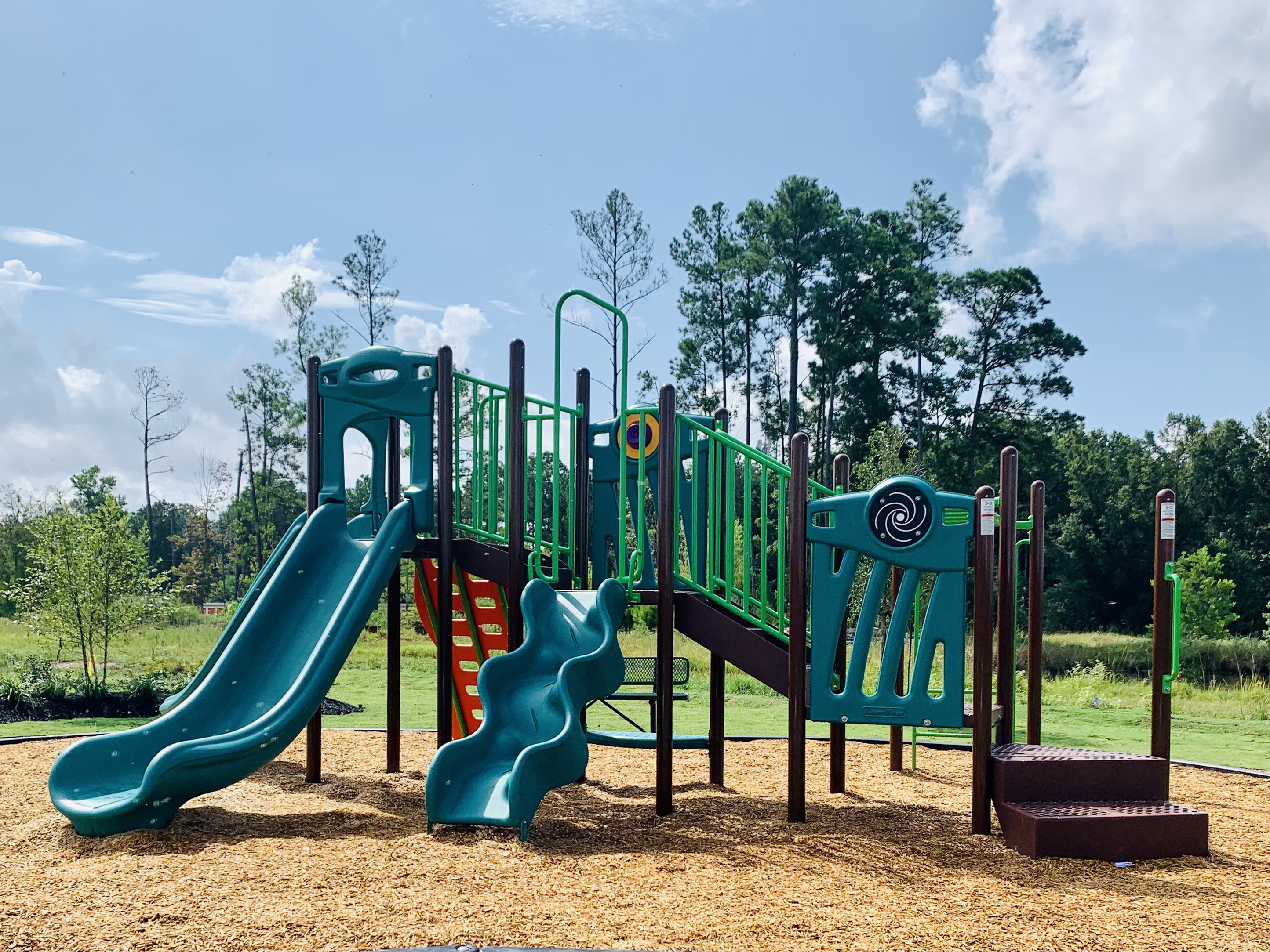 Charming playground with vibrant slides and climbing structures set against a lush, green park backdrop.