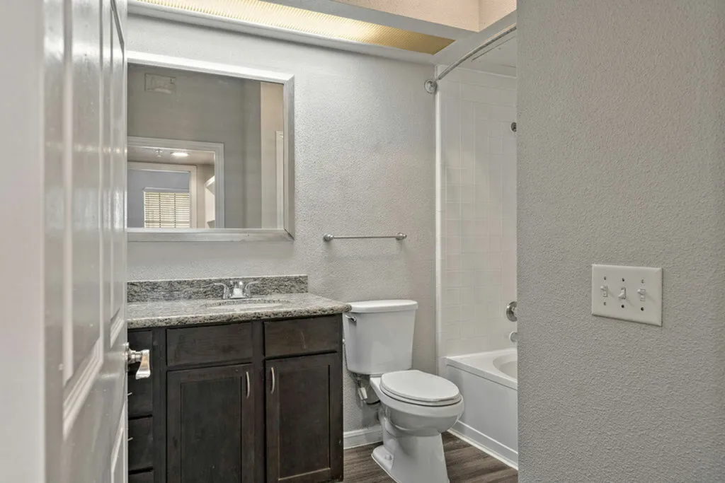 Modern bathroom with sleek granite countertop, elegant dark wood cabinetry, and a pristine bathtub set against a stylish neutral palette.