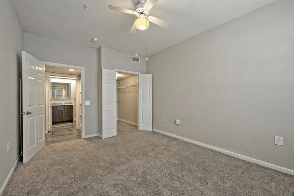 Bright and spacious bedroom with plush carpeting, ceiling fan, and open doorway leading to a modern bathroom and large walk-in closet.