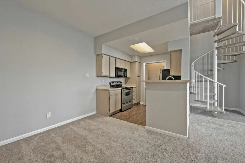 Modern apartment kitchen with stainless steel appliances, cozy carpeted living area, and elegant spiral staircase.