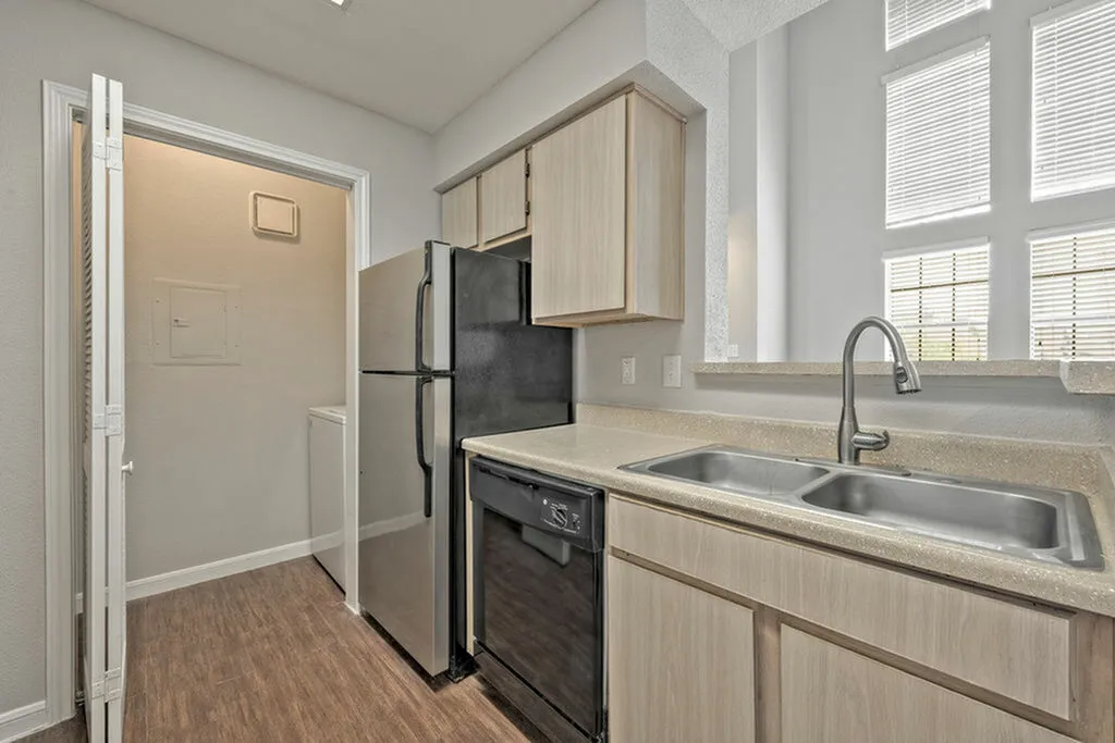 Modern kitchen featuring sleek countertops, double sink, and a black refrigerator with adjacent laundry area.