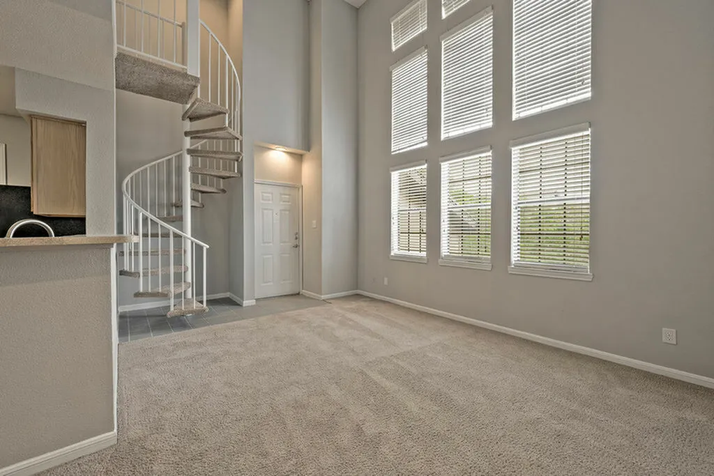 Elegant living room with high ceilings and spiral staircase, featuring large windows for natural light.
