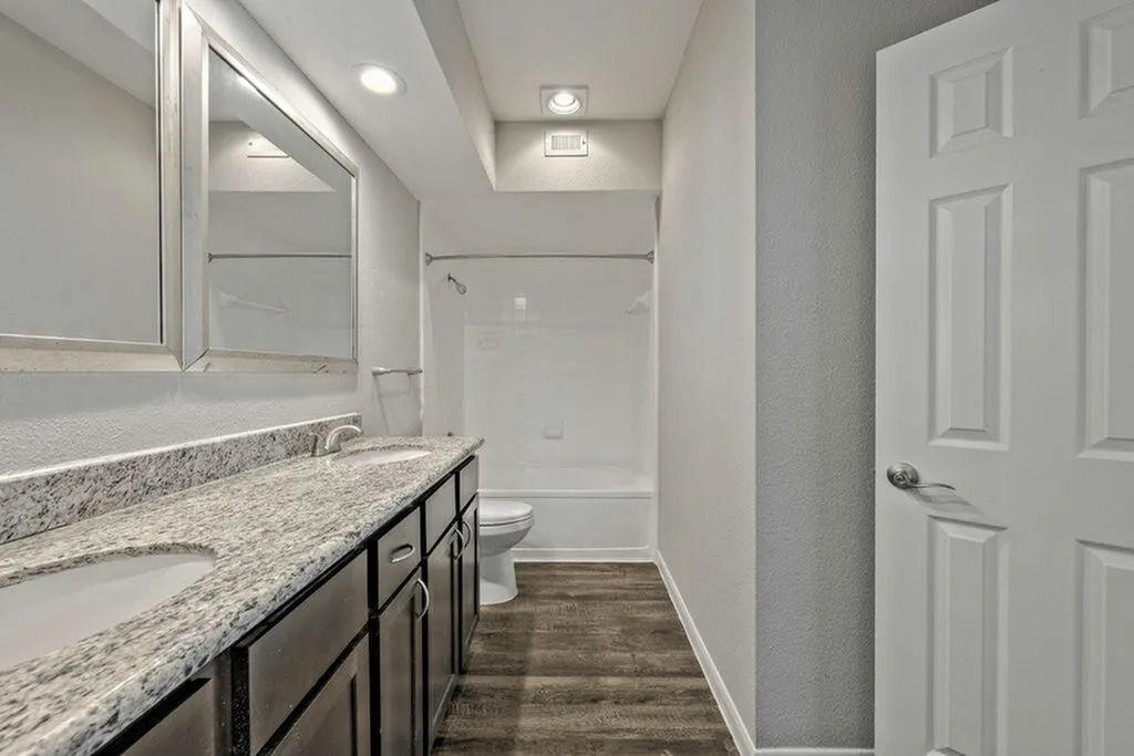 Elegant bathroom featuring granite countertops, double sinks, and a modern bathtub with sleek cabinetry.