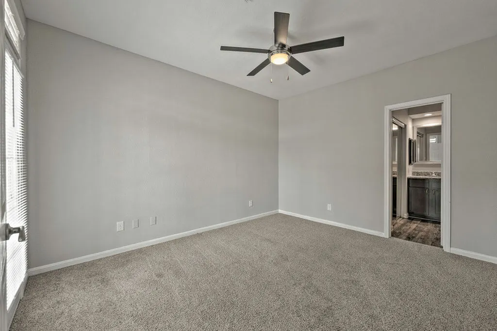 Bright and spacious room with plush carpeting, modern ceiling fan, and ensuite bathroom access.