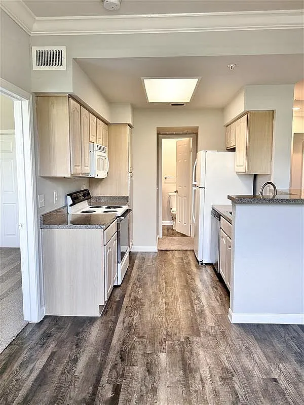 Bright kitchen with modern appliances, light wood cabinetry, and sleek countertops leading to a convenient bathroom, featuring stylish flooring and ample space for culinary creativity.