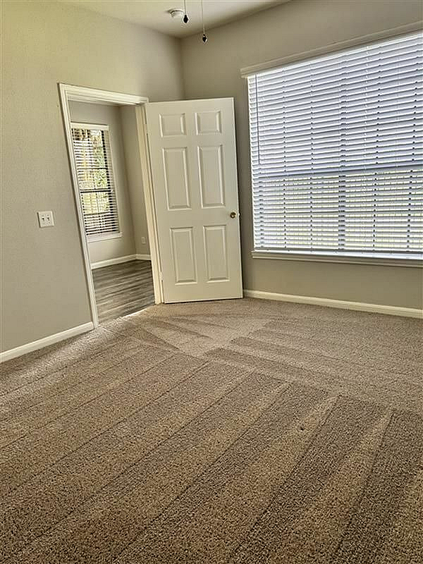 Bright and spacious bedroom with fresh carpet flooring, ample natural light through large windows, and a connected additional room offering versatile use.