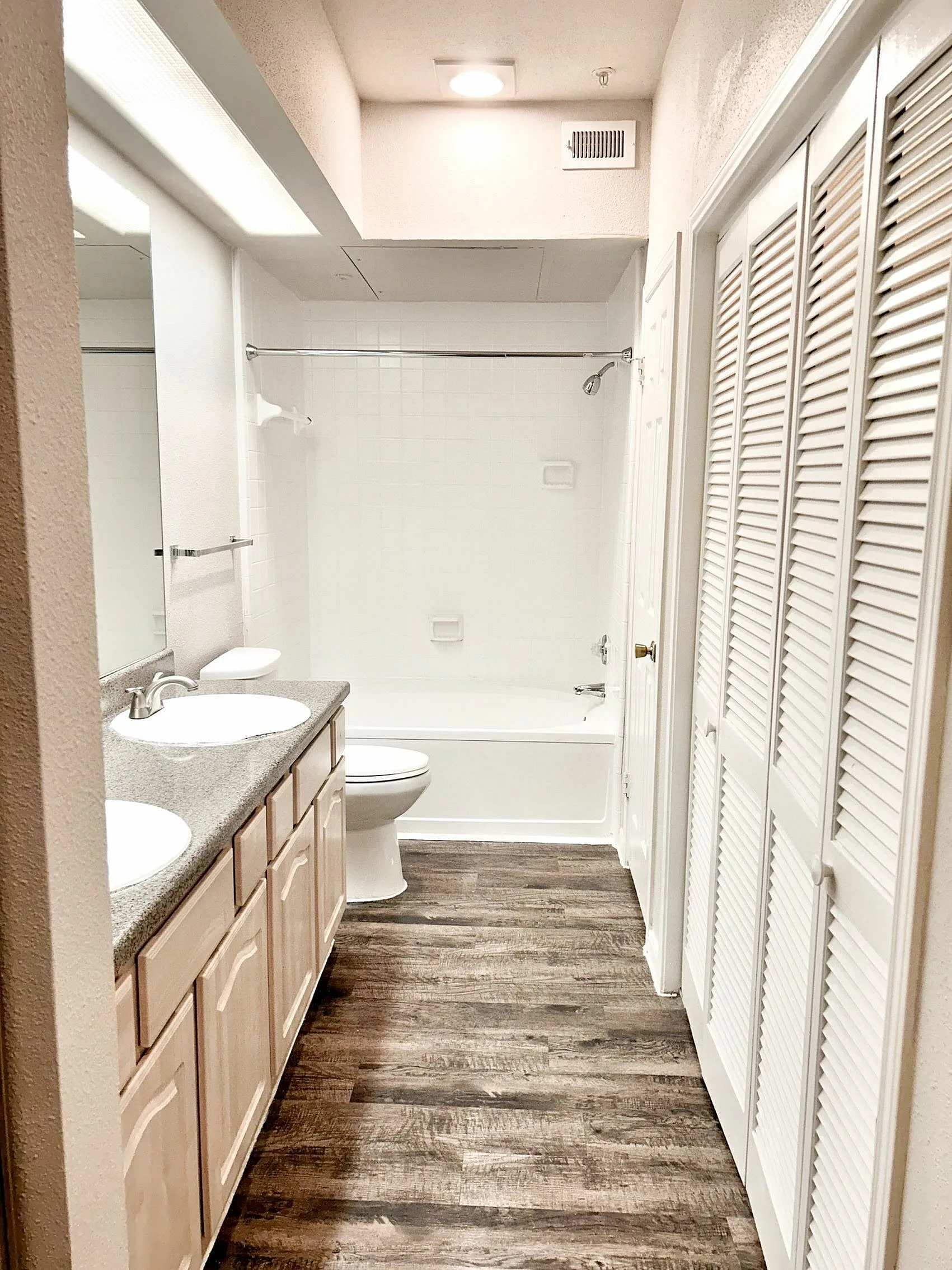 Bright and spacious bathroom featuring a modern double vanity, elegant lighting, and sleek hardwood floors.