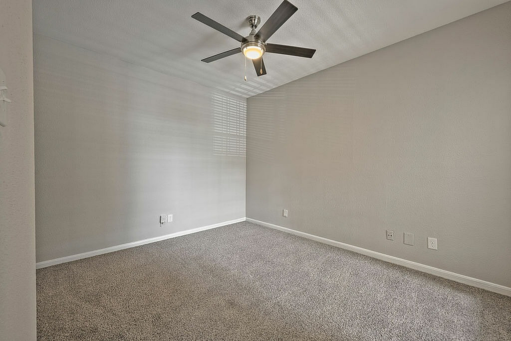 Spacious empty bedroom with plush carpeting and modern ceiling fan, perfect for customization and personal touch.