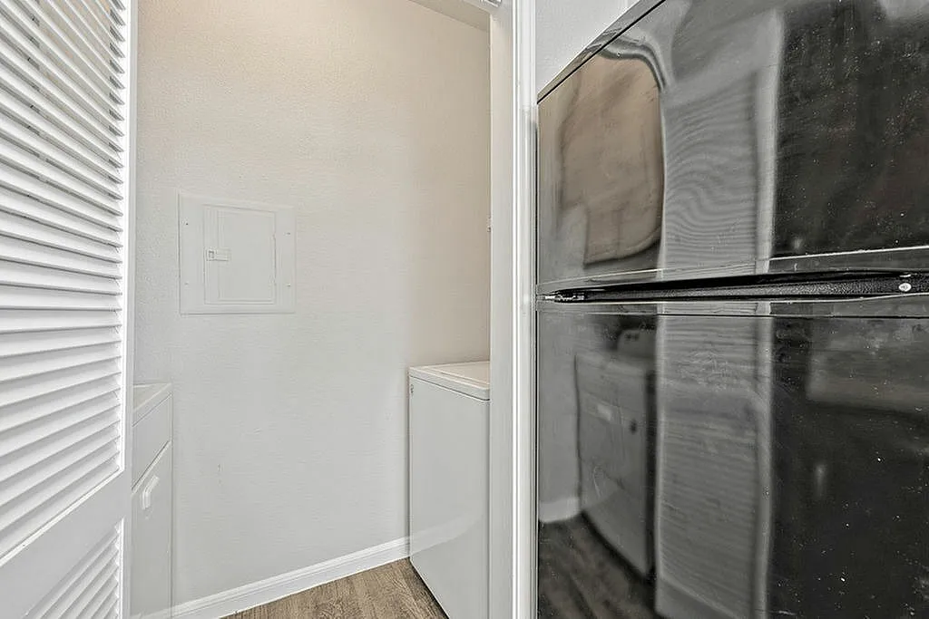 Compact laundry area with modern washer and dryer, adjacent to a sleek black refrigerator, in a bright and clean apartment setting.