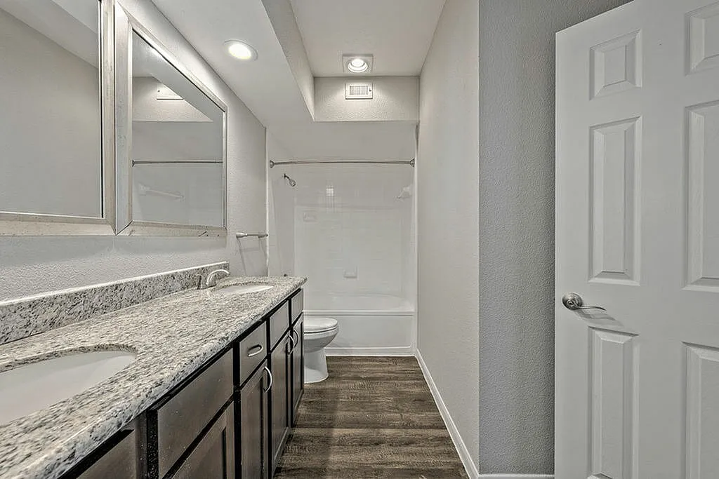 Sleek modern bathroom featuring dual granite sinks, elegant mirrors, and rich wooden cabinetry.