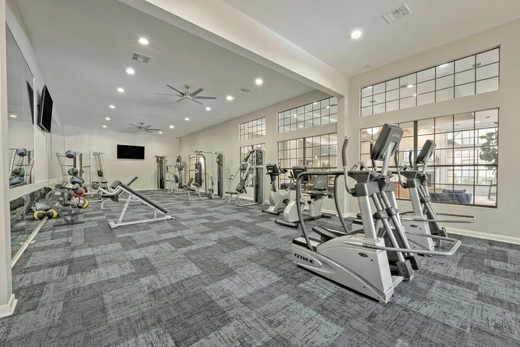 Modern fitness center with new, state-of-the-art exercise equipment, spacious layout, and large windows providing natural light.