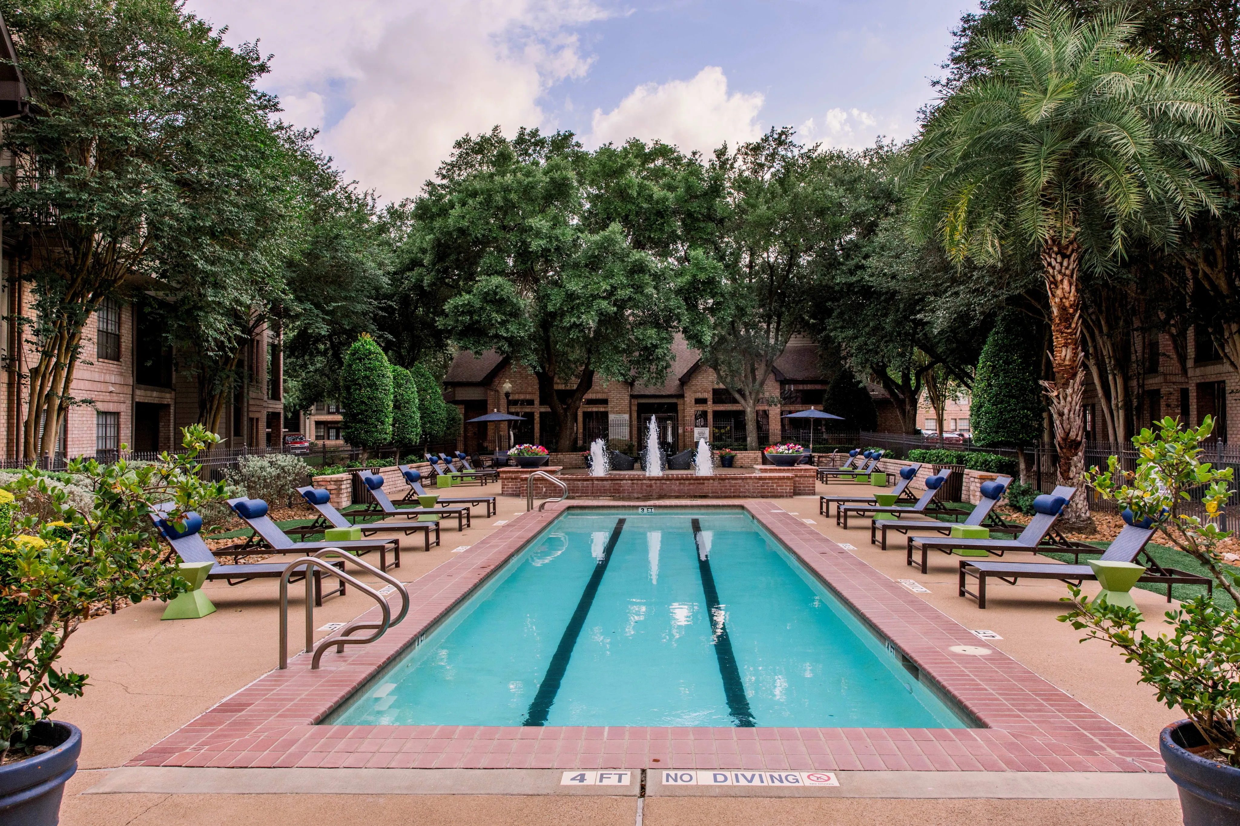 Luxurious apartment complex featuring a refreshing outdoor pool surrounded by elegant lounge chairs and lush greenery.