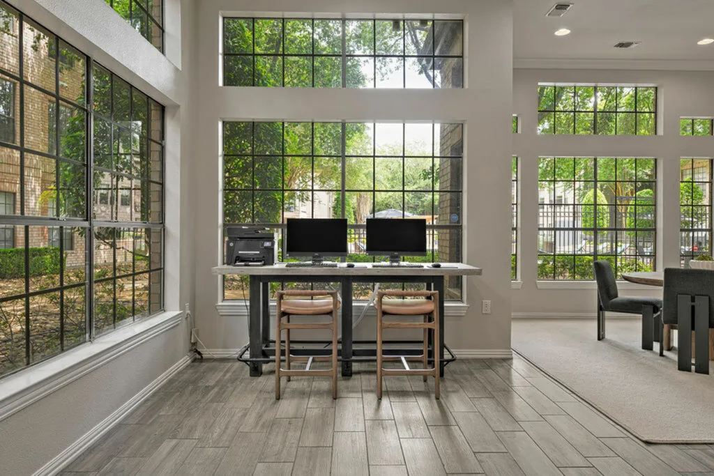 Bright and airy office space with expansive windows showcasing lush greenery outside, featuring modern desks and elegant seating, creating a serene work environment.