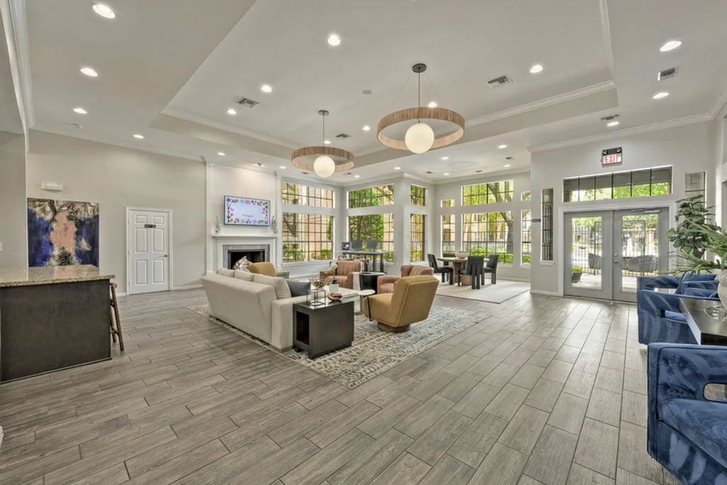 Spacious and elegant apartment lounge featuring modern furnishings, a cozy fireplace, and abundant natural light through large windows.