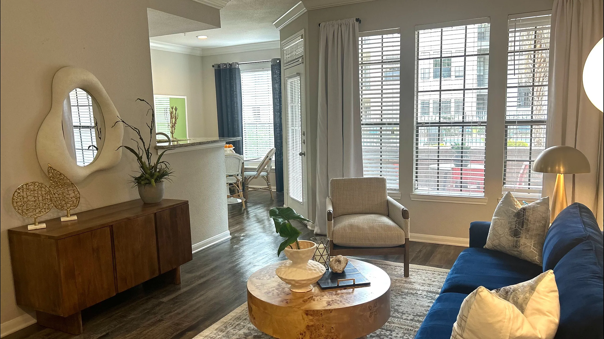 Elegant living room with a plush blue sofa, modern decor, and abundant natural light from large windows.