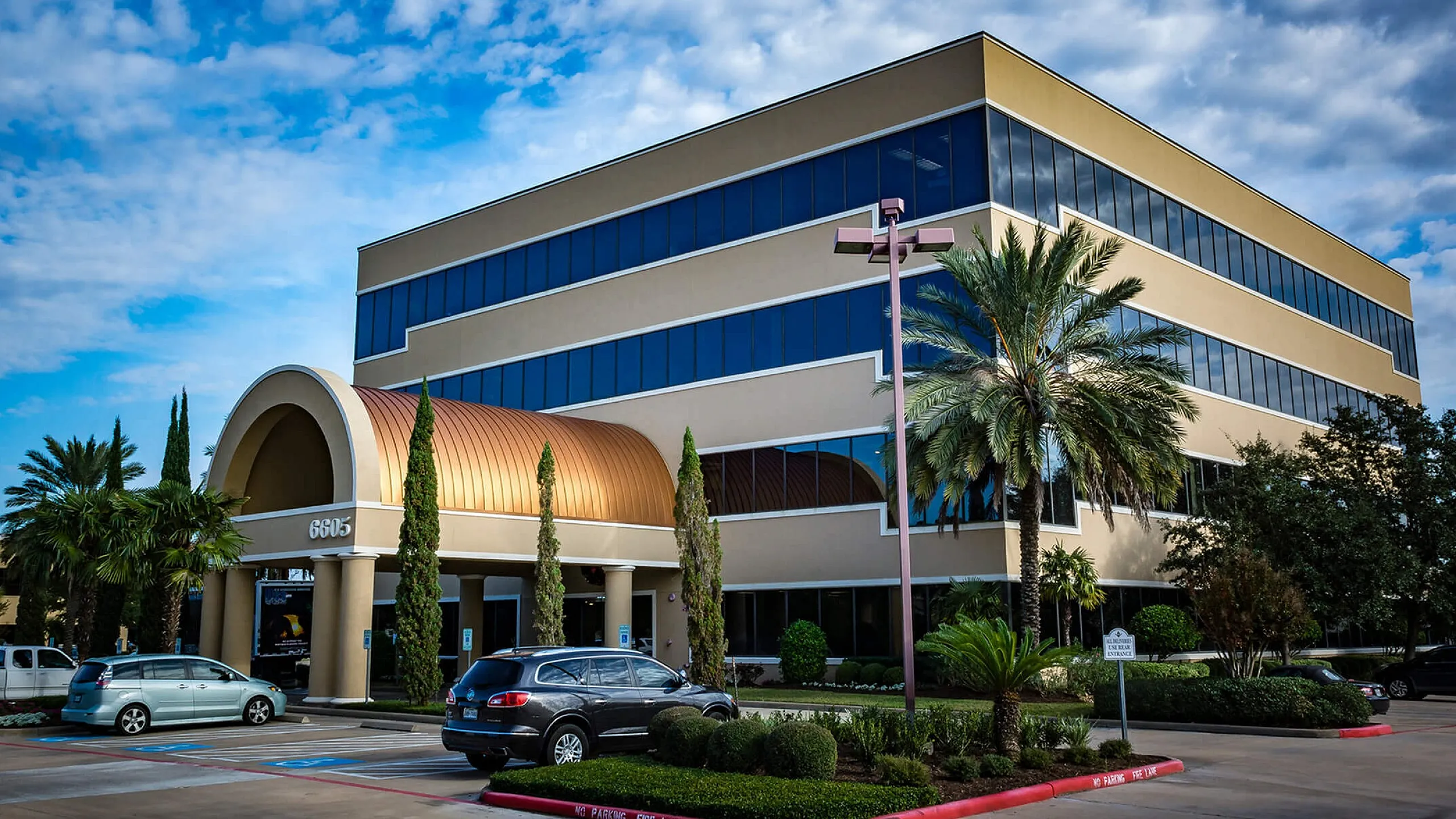 Modern commercial building with a stylish arched entrance, surrounded by palm trees and well-maintained landscaping under a vibrant blue sky.