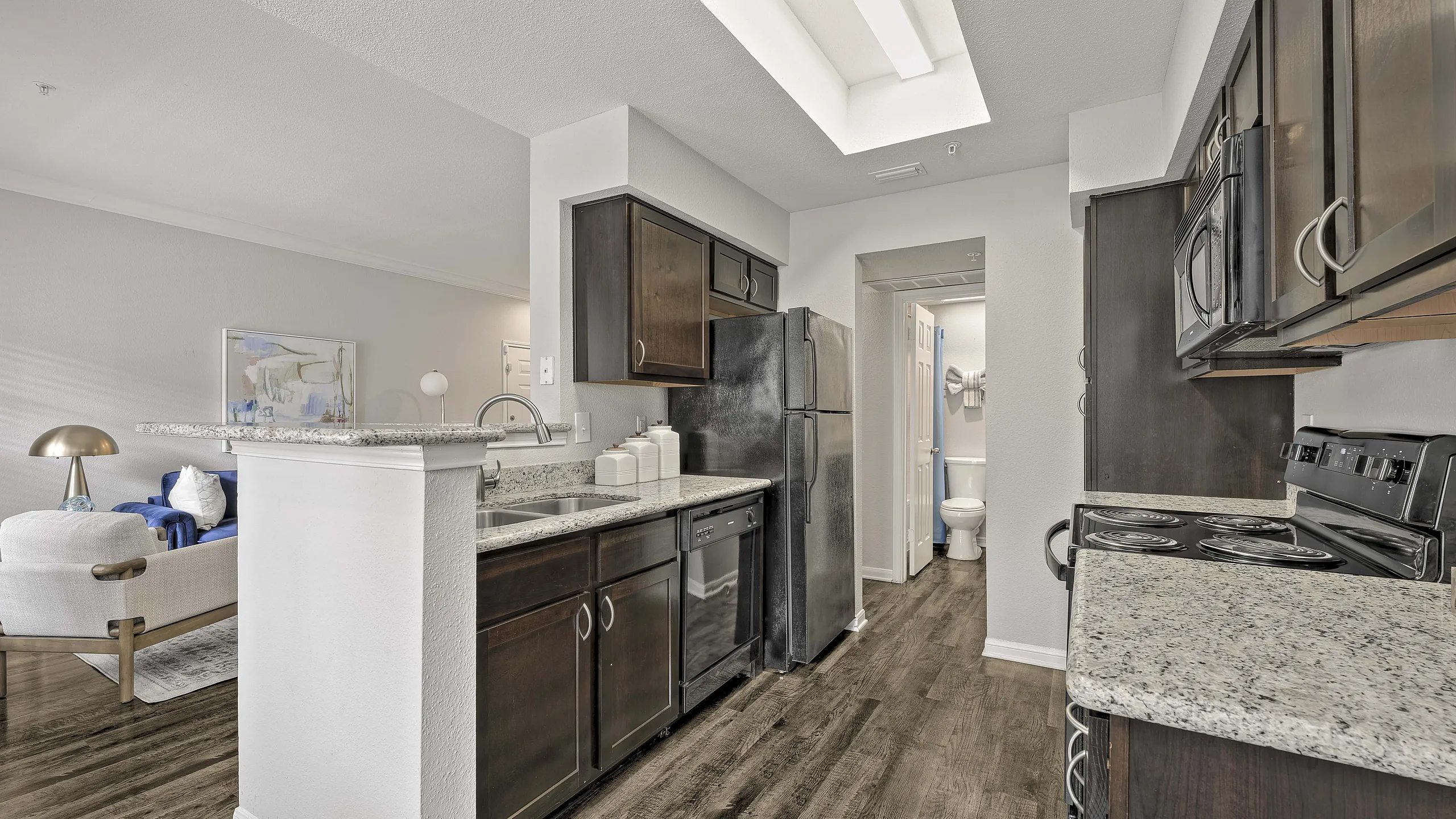 Modern kitchen with sleek granite countertops and dark wood cabinetry, open to a stylish living area featuring elegant decor and a plush sofa.