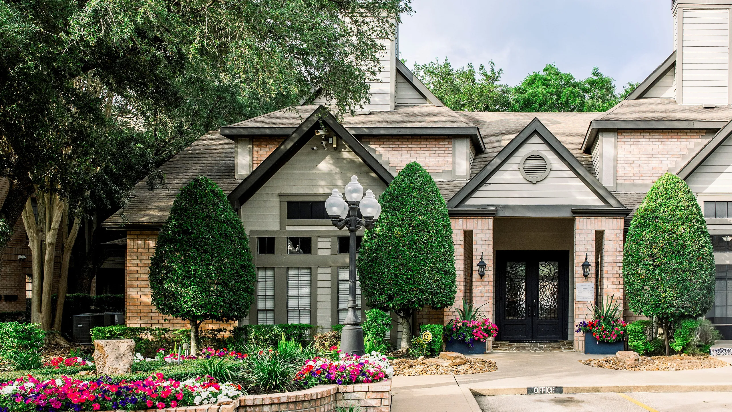 Inviting rustic-style apartment building with lush landscaping, vibrant flowerbeds, and charming brick detailing.