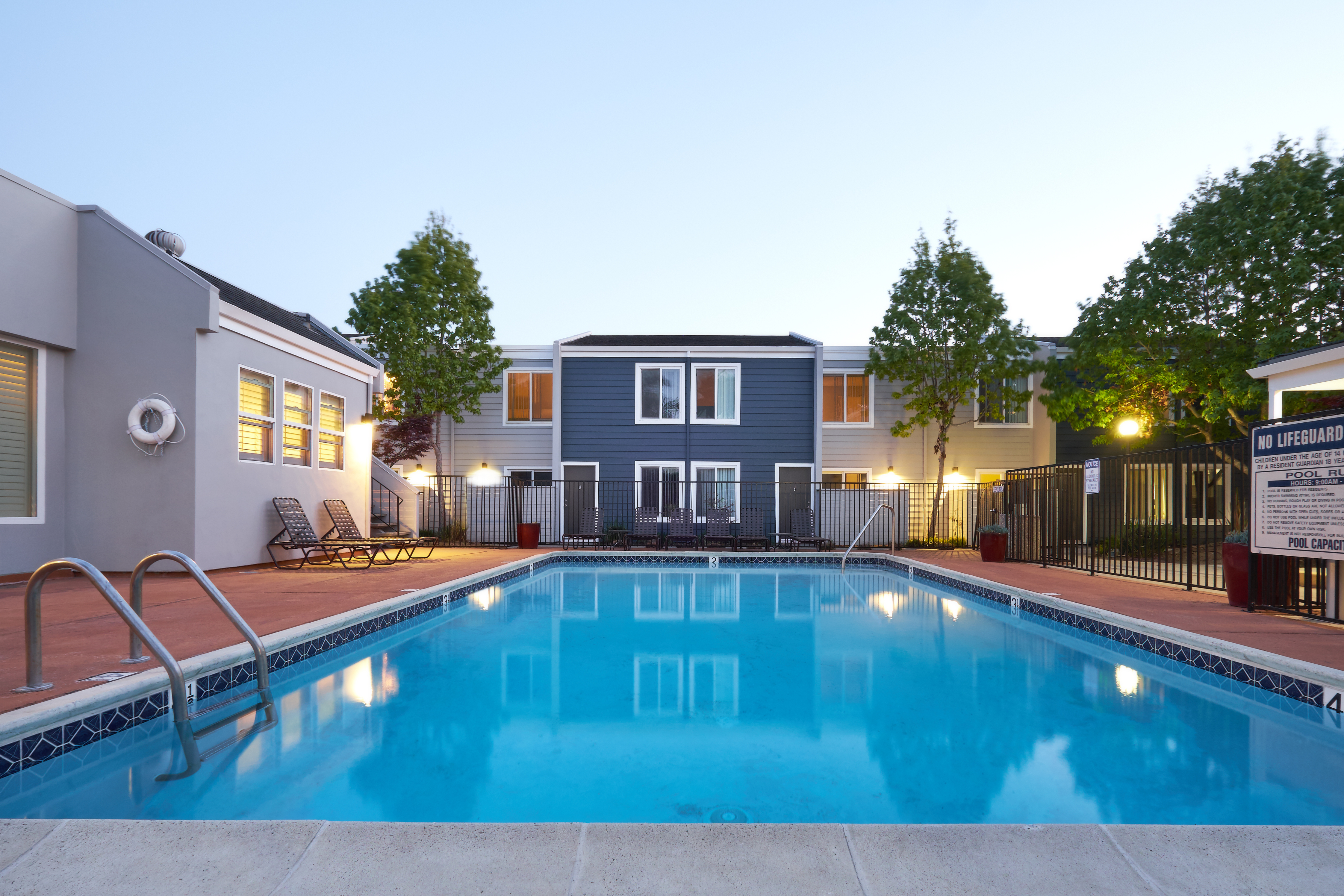 Inviting apartment community featuring a sparkling swimming pool, modern architecture, and lush greenery under a serene sky.