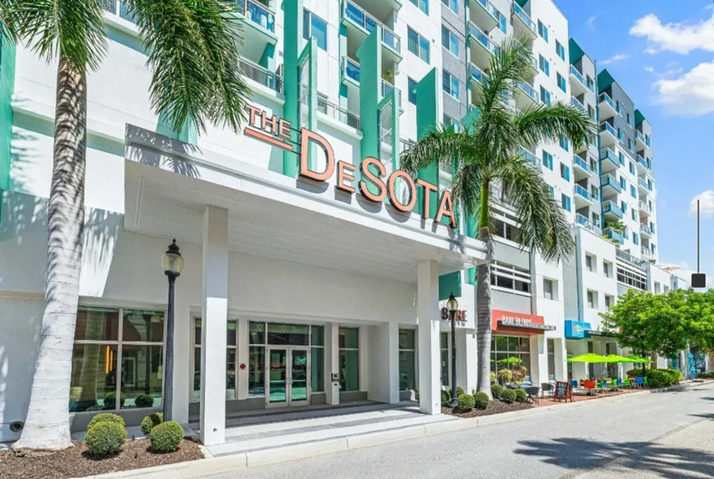 Exterior photo of The DeSOTA luxury apartment building in downtown Sarasota, Florida, featuring palm trees and street-level shops.