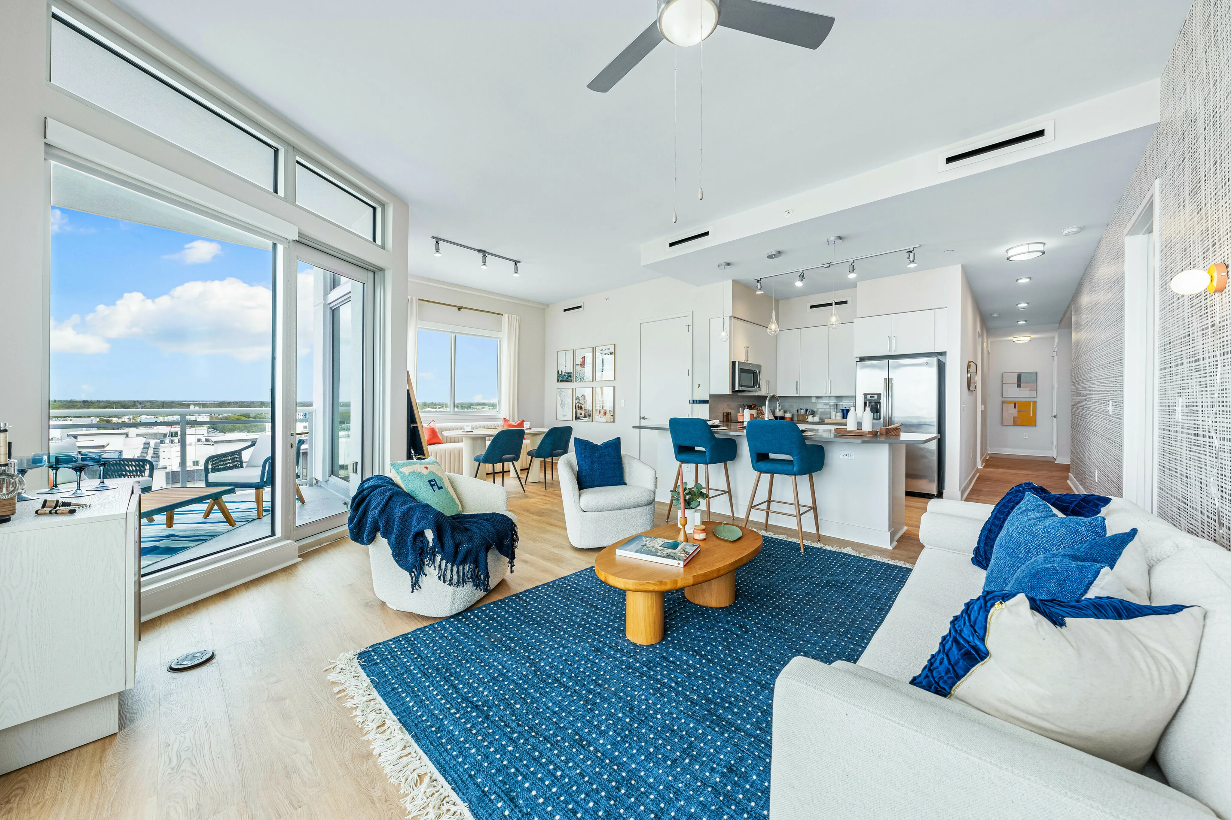 Bright open-plan living room featuring floor-to-ceiling windows, cozy seating area, modern kitchen with sleek bar stools, and stunning views.